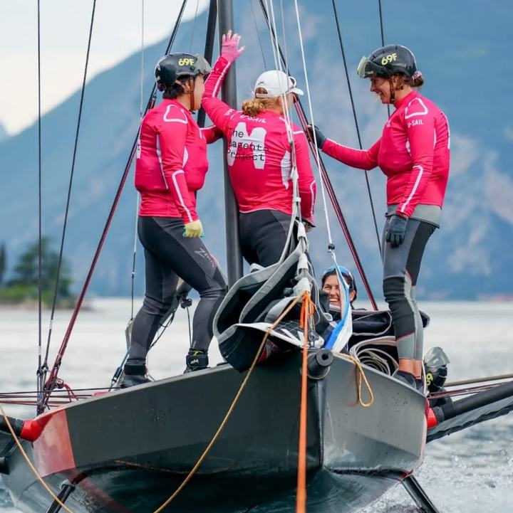 The Magenta Project crew in pink on a foiling sailboat
